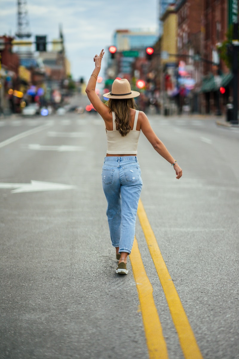 Photo by Moncell Allen woman in blue denim jeans and brown hat walking on the street during daytime